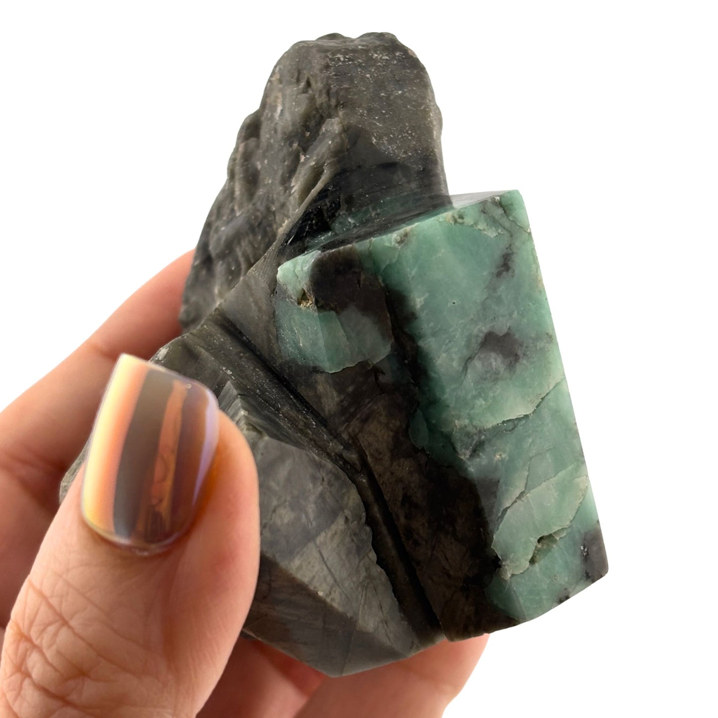 Polished emerald on black rock in hand