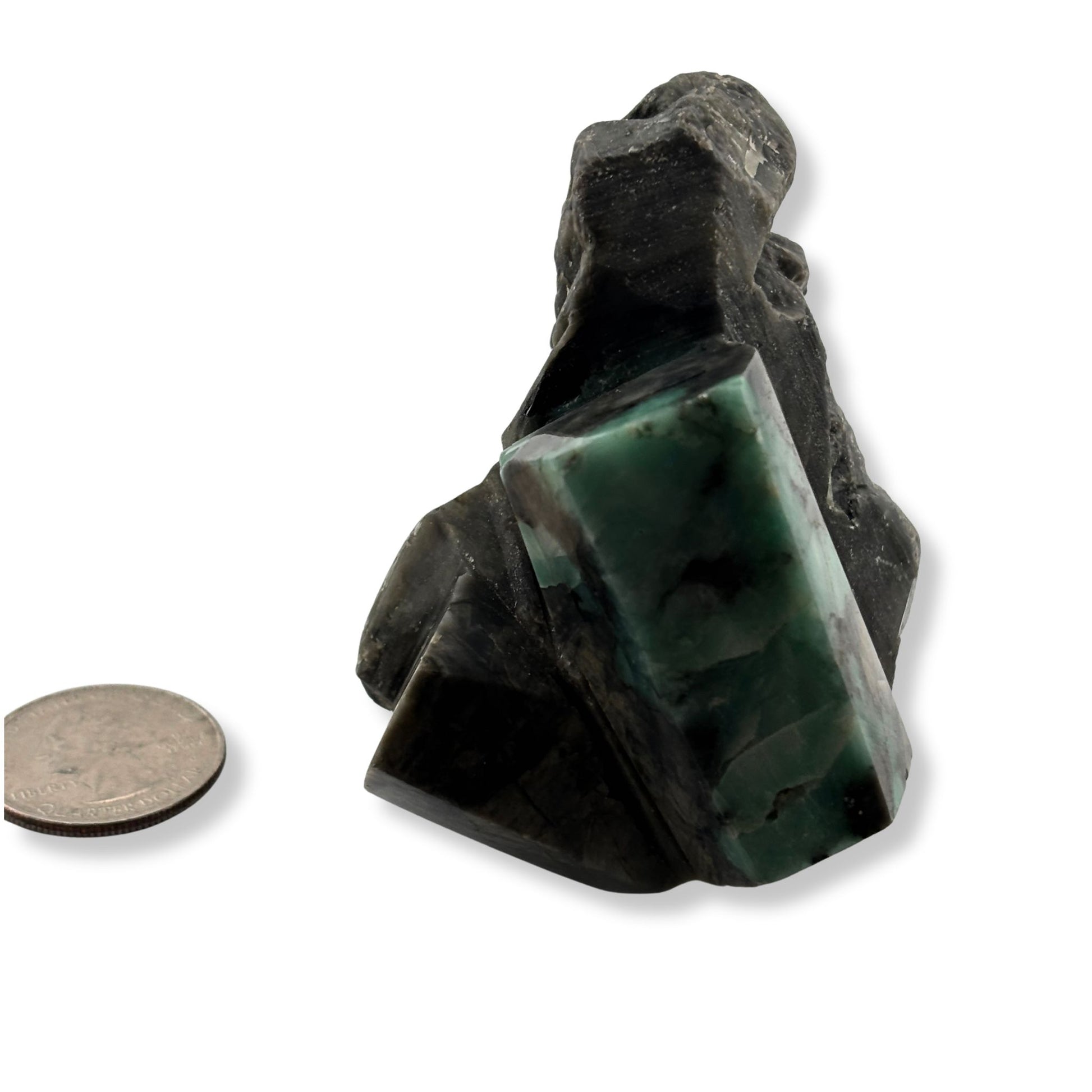 Polished emerald next to quarter for size comparison showing piece is larger than coin. 