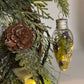 Decorative light bulb ornament with natural elements hanging on a tree.